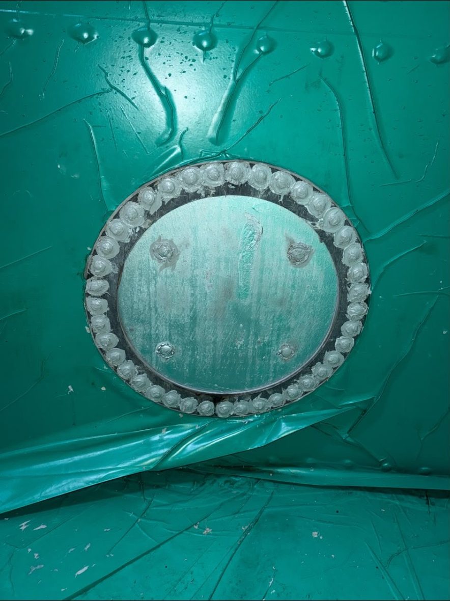 Circular bolted manway cover set into a green lined tank wall