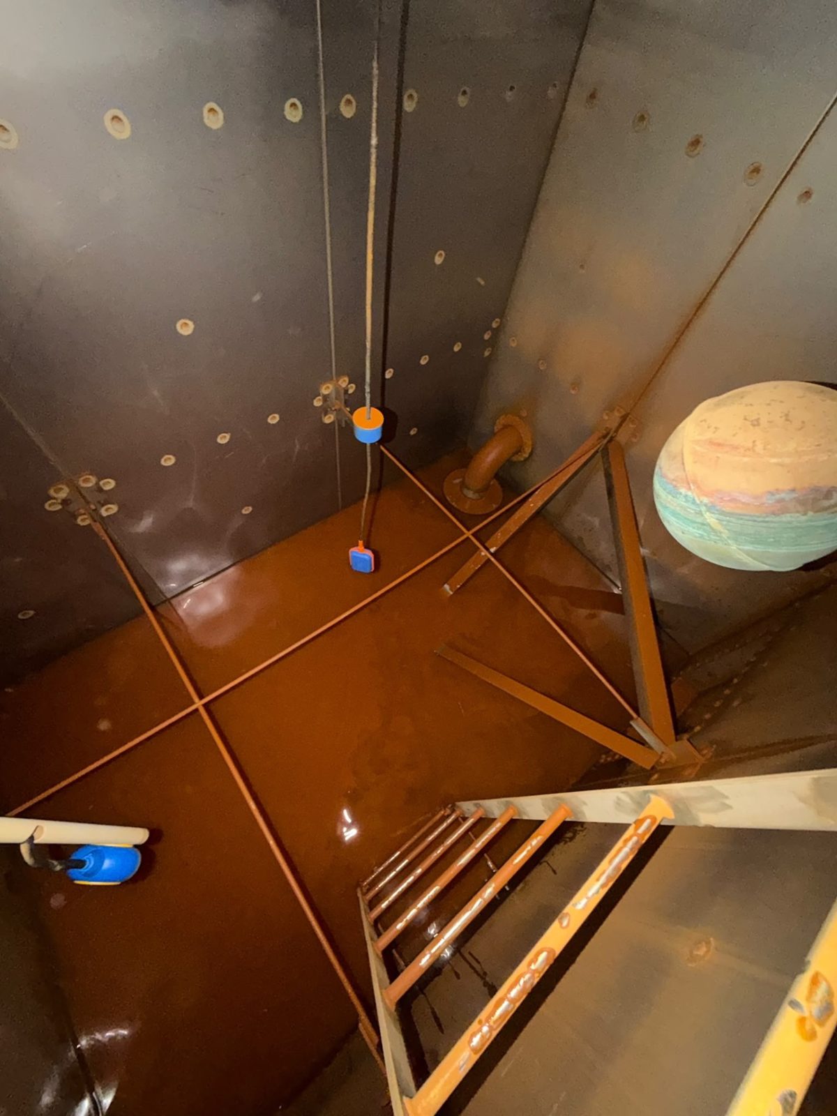 Steel tank interior with access ladder, bracing and stained floor surface